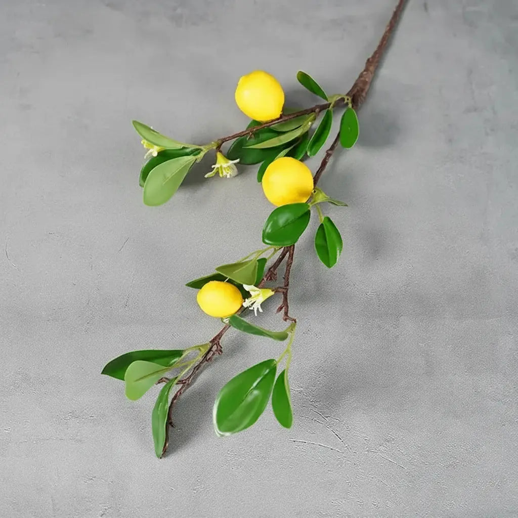 Artificial lemon branch with green leaves and three yellow lemons.